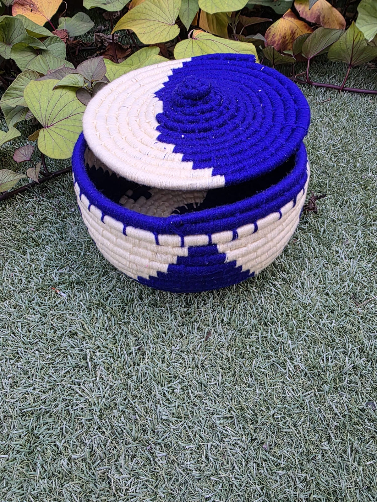 A handwoven basket with a matching lid, featuring a bold blue and off-white geometric pattern.