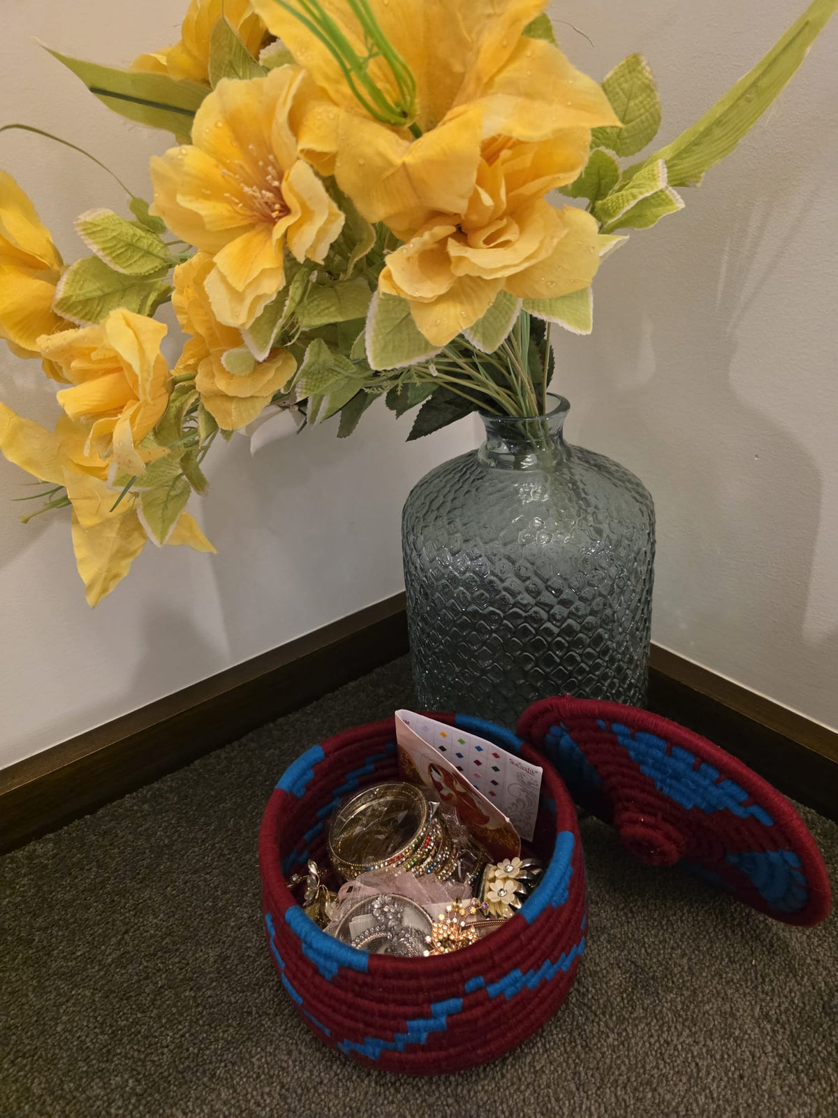 A round woven basket with a matching lid, filled with jewelry and a card.