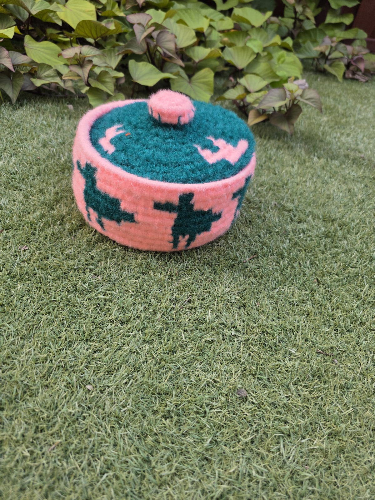 A small hand-knit lidded basket or pot in pink and teal.